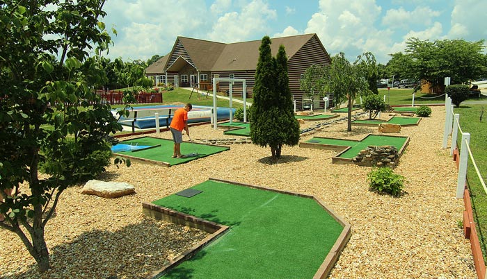 person playing mini-golf with large cabin and trees behind